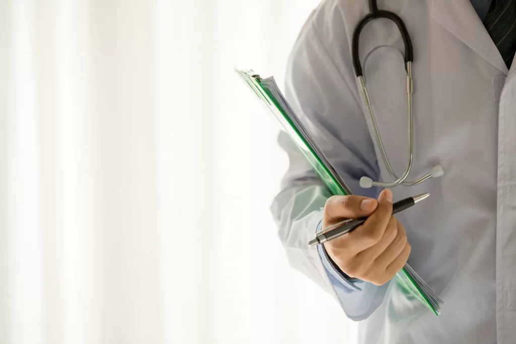 Profesional de la salud sosteniendo documentos y bolígrafo, reflejando el trato personalizado en la atención clínica.
