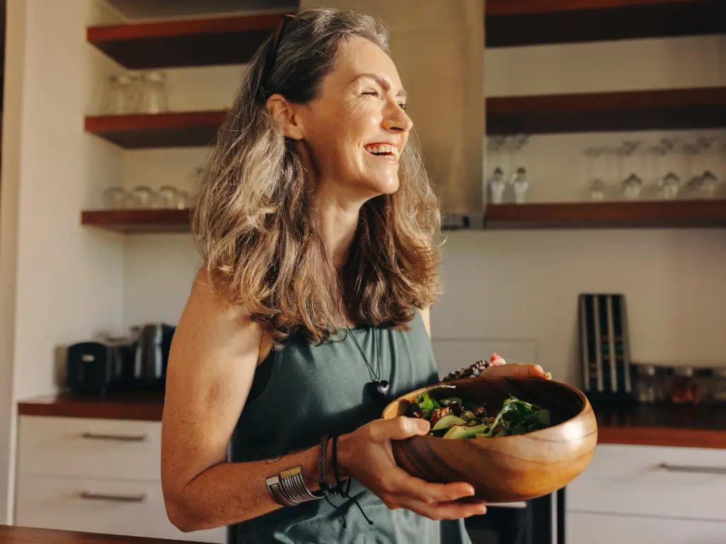 Mujer sonriente sosteniendo un bowl de ensalada como ejemplo de una alimentación saludable dentro de la nutrición oncológica.
